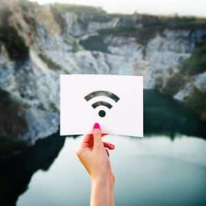 A person holds up an image of a wifi signal in front of a beautiful landscape